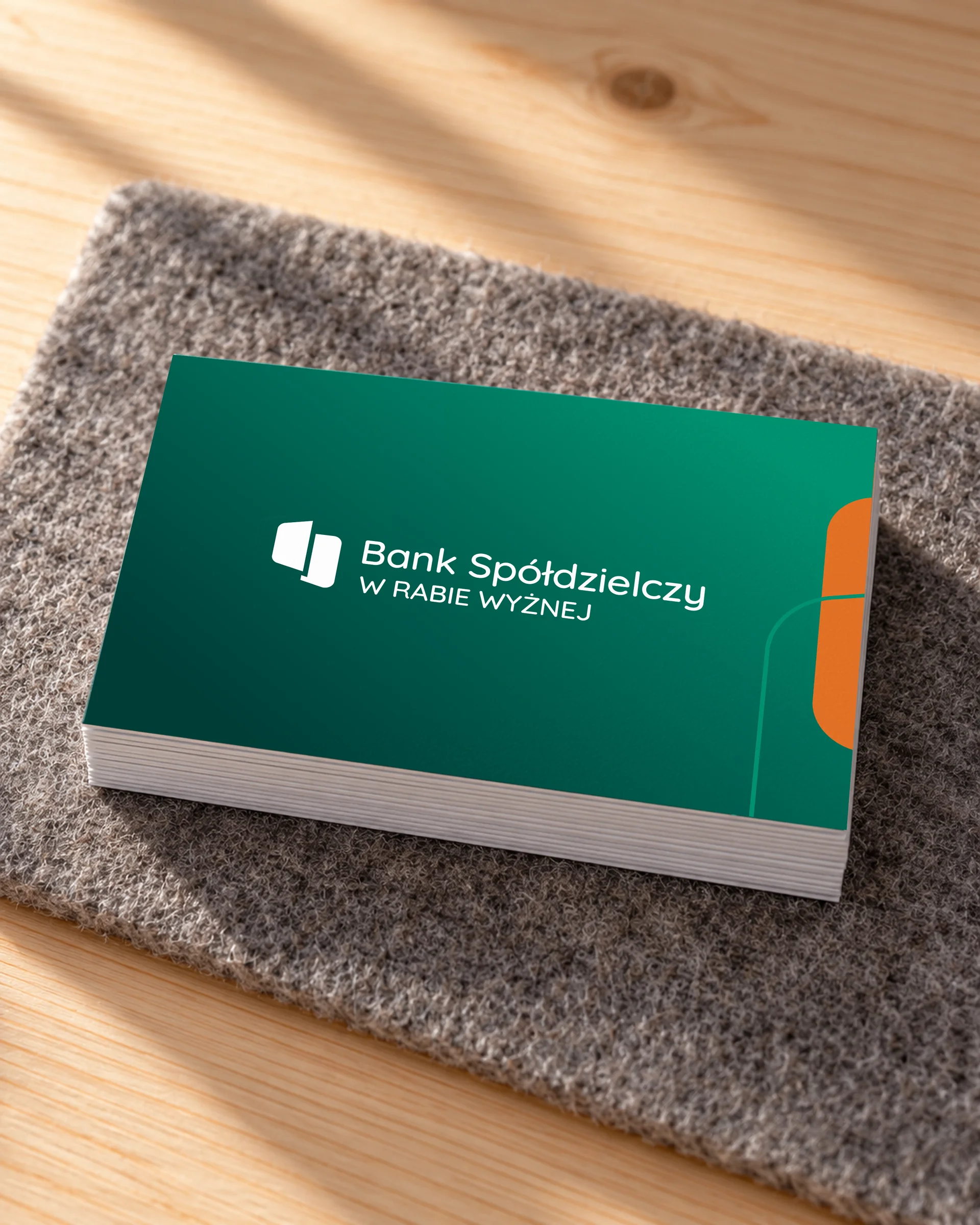 Stos zielonych wizytówek banku z białym logo na wełnianym filcu