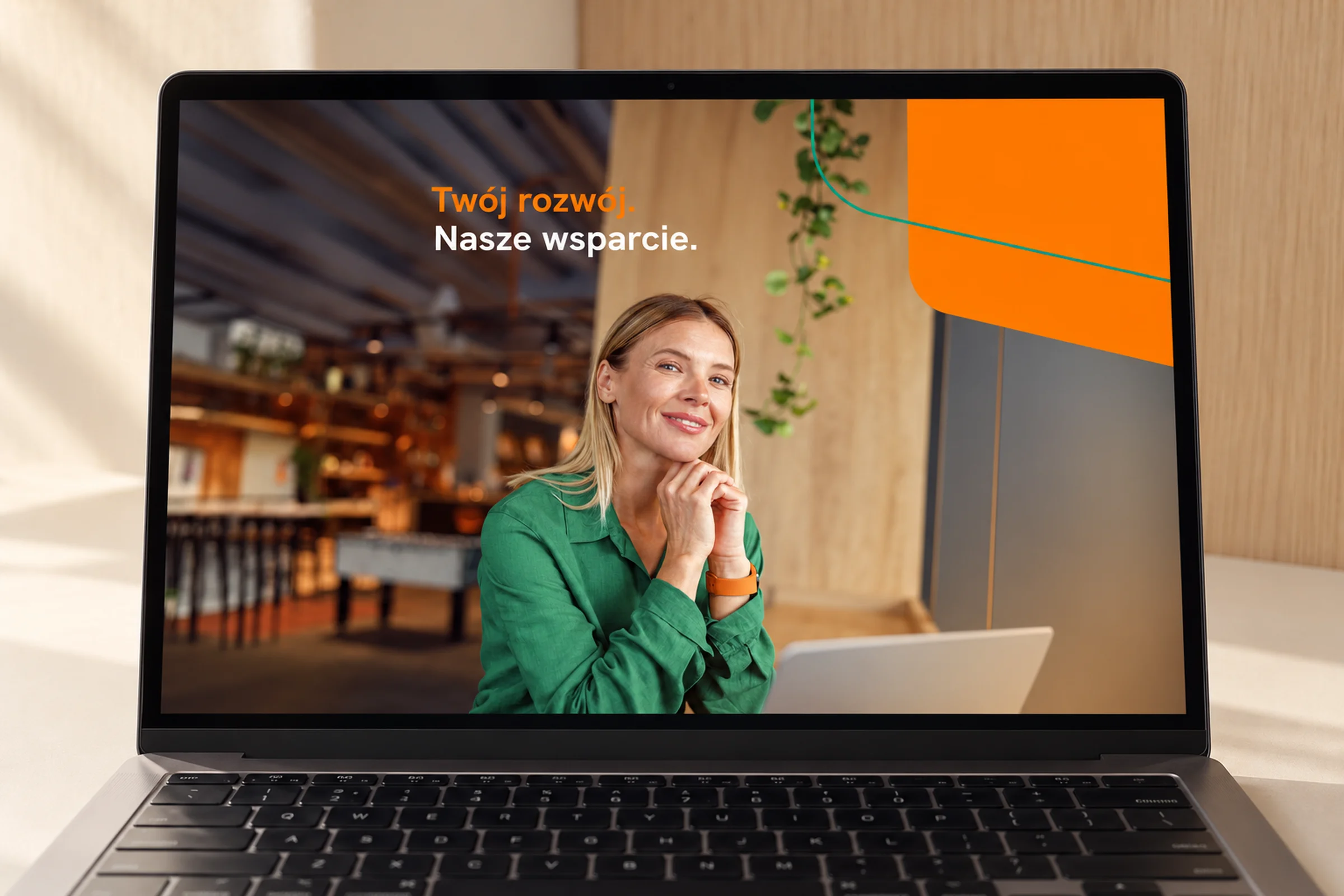 Laptop z grafiką strony logowania banku: kobieta w zielonej koszuli i hasło „Twój rozwój. Nasze wsparcie.”