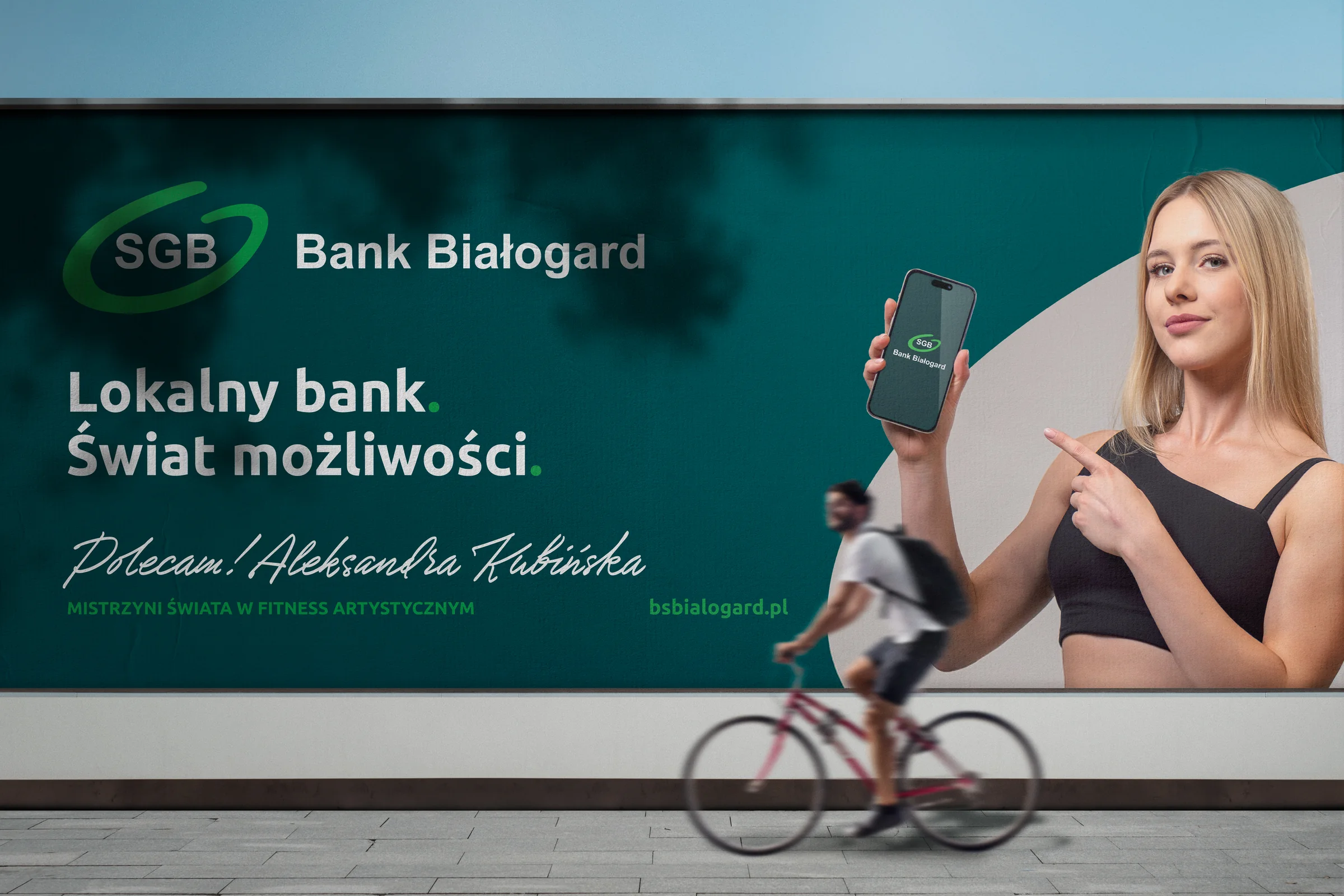 Billboard Banku Białogard z hasłem „Lokalny bank. Świat możliwości.” i poleceniem Aleksandry Kubińskiej, przed nim przejeżdża rowerzysta